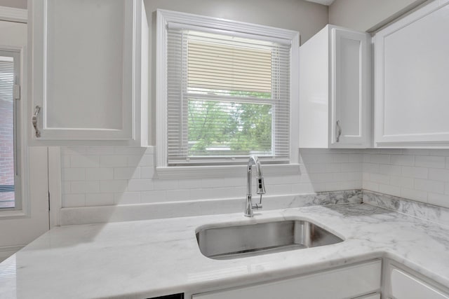 kitchen featuring white cabinets, light stone counters, decorative backsplash, and a sink