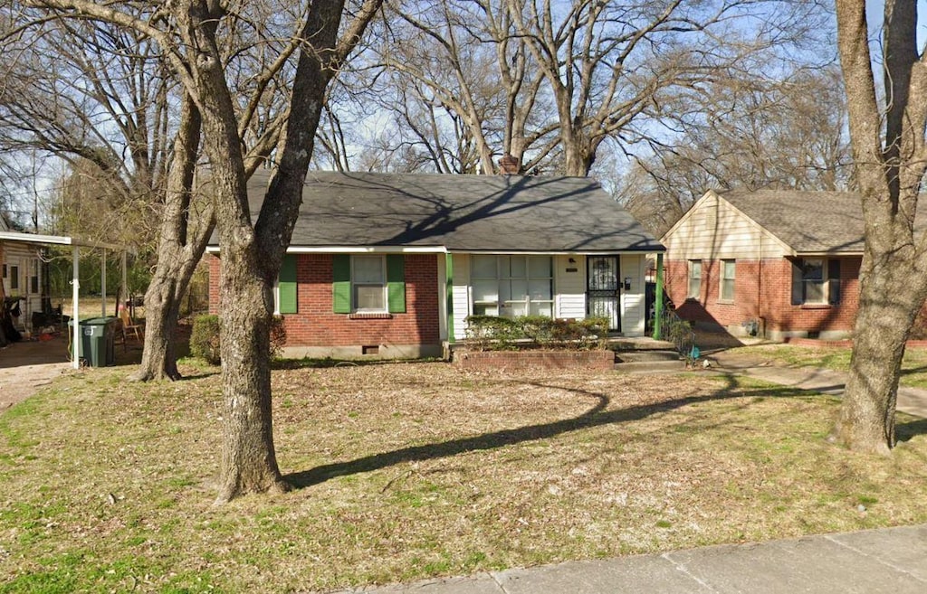 ranch-style house with a chimney, roof with shingles, a front yard, a carport, and brick siding