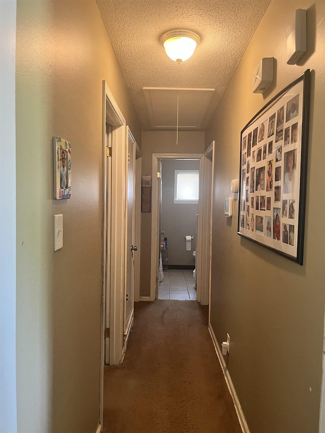 hall with attic access, a textured ceiling, tile patterned floors, and carpet