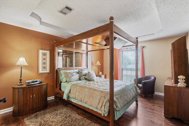 bedroom with visible vents, a textured ceiling, baseboards, and wood finished floors