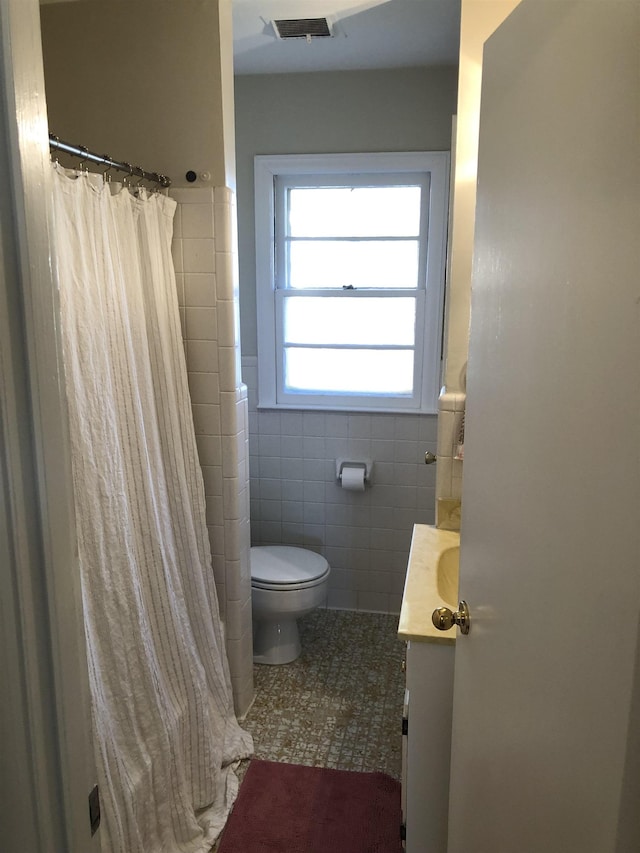 bathroom with vanity, visible vents, toilet, tile walls, and a wainscoted wall