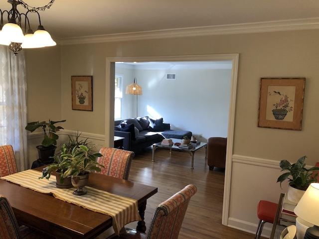 dining space featuring crown molding, a chandelier, wood finished floors, and visible vents
