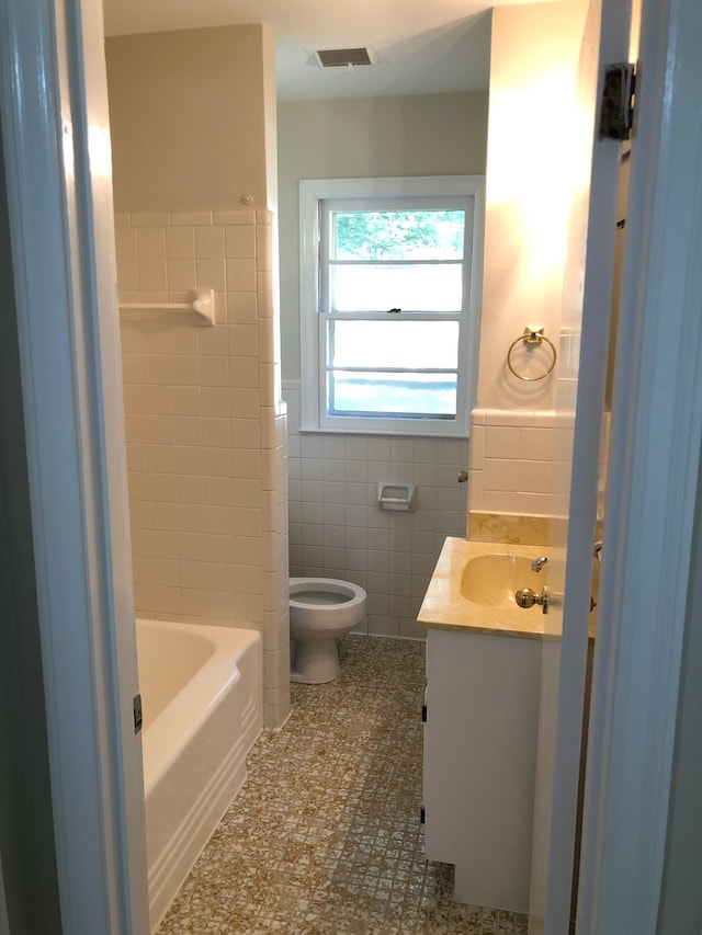 bathroom with wainscoting, vanity, toilet, tile walls, and visible vents