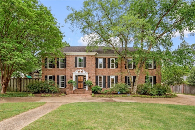 colonial inspired home with fence, a front lawn, and brick siding