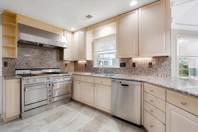 kitchen with wall chimney range hood, stainless steel appliances, a sink, and cream cabinets