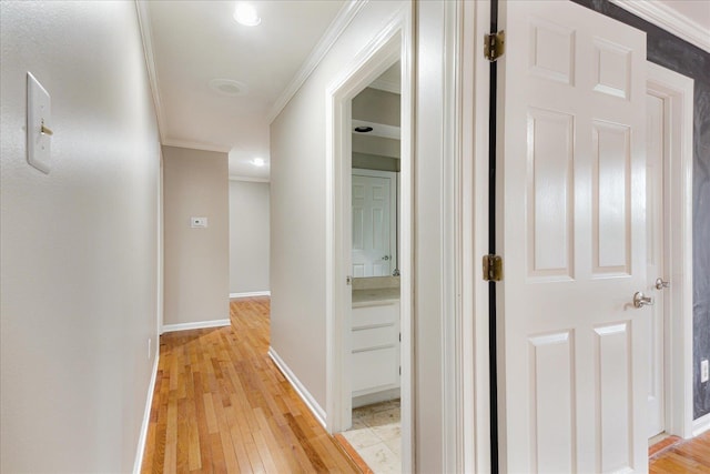 hallway featuring baseboards, ornamental molding, and light wood-type flooring