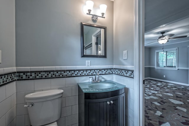half bath with ceiling fan, tile walls, a wainscoted wall, vanity, and toilet