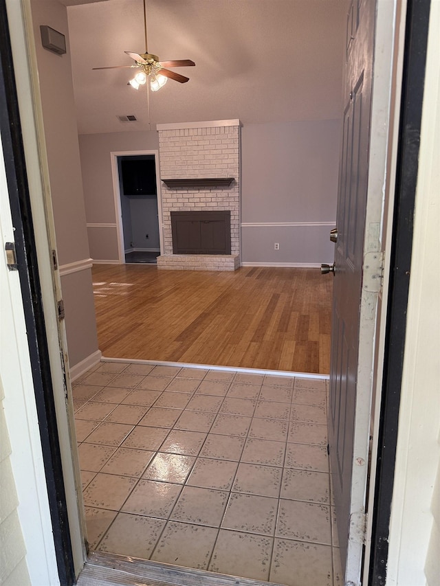unfurnished living room featuring baseboards, a brick fireplace, light wood finished floors, and ceiling fan