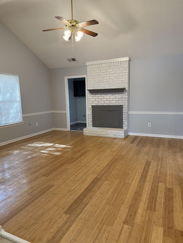 unfurnished living room with ceiling fan, visible vents, vaulted ceiling, a brick fireplace, and light wood-style flooring