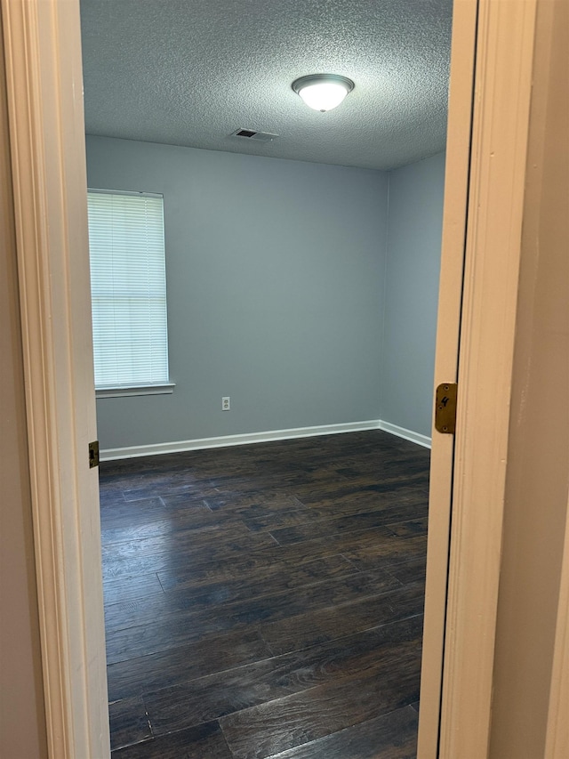unfurnished room featuring baseboards, a textured ceiling, dark wood-style floors, and visible vents