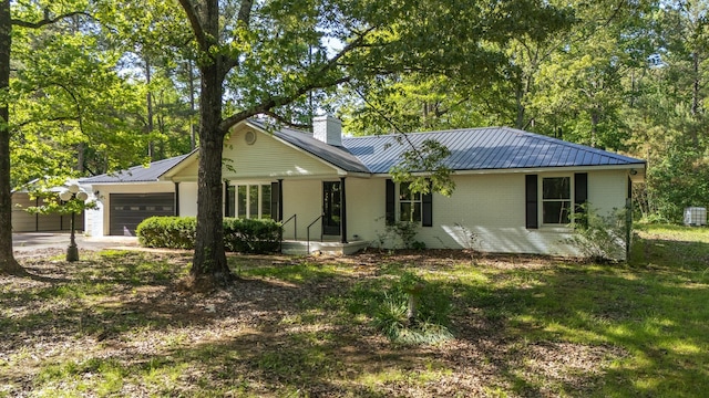 single story home with a chimney, brick siding, metal roof, an attached garage, and driveway