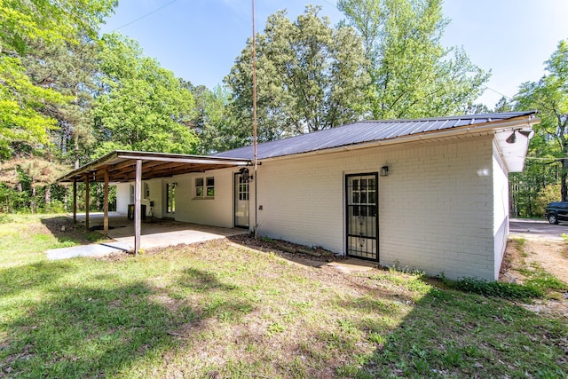 back of house with brick siding, a patio area, a carport, a yard, and metal roof