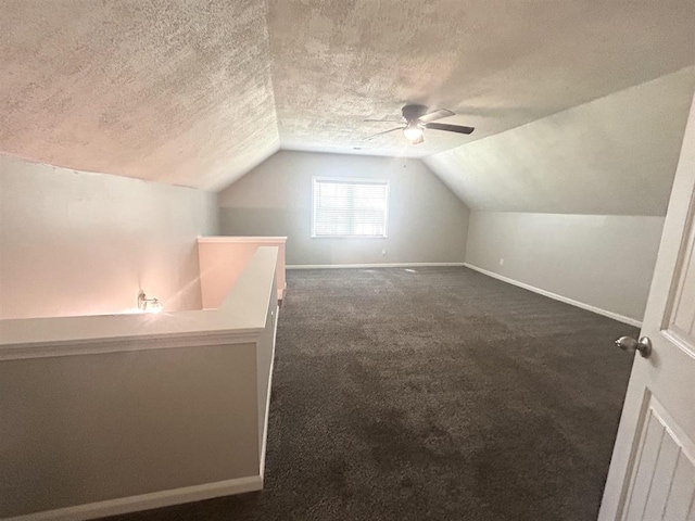 additional living space featuring a ceiling fan, a textured ceiling, vaulted ceiling, baseboards, and dark carpet