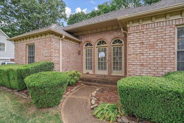 property entrance featuring roof with shingles and brick siding
