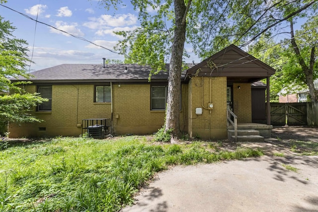 rear view of house with fence, roof with shingles, brick siding, a gate, and central air condition unit