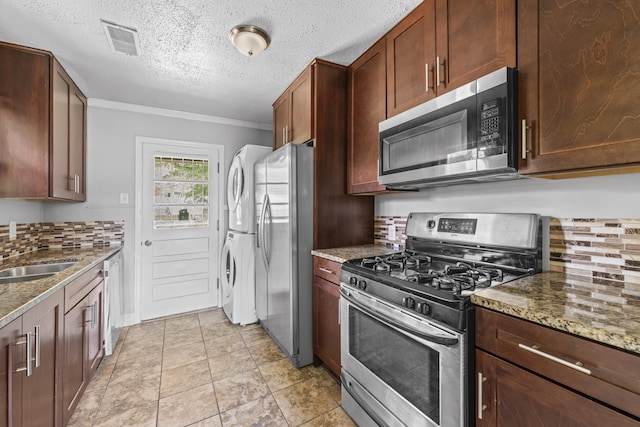kitchen featuring stacked washer / drying machine, a sink, stainless steel appliances, backsplash, and visible vents