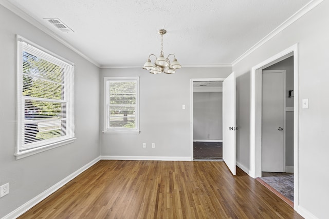 unfurnished dining area with visible vents, ornamental molding, an inviting chandelier, wood finished floors, and baseboards