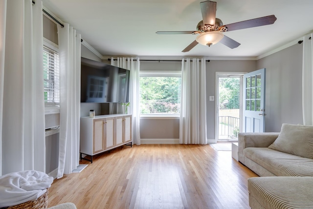 living area featuring light wood-type flooring, a ceiling fan, baseboards, and ornamental molding