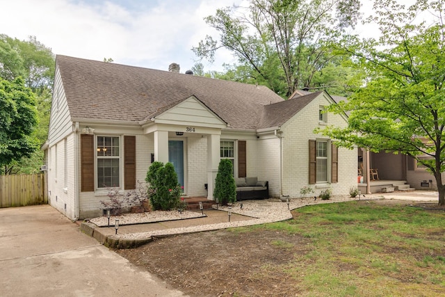 view of front of house featuring brick siding, fence, and a shingled roof
