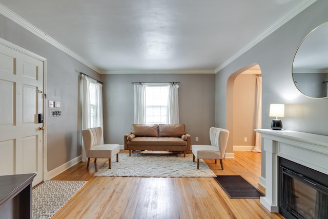 living area featuring crown molding, arched walkways, a fireplace, baseboards, and light wood finished floors