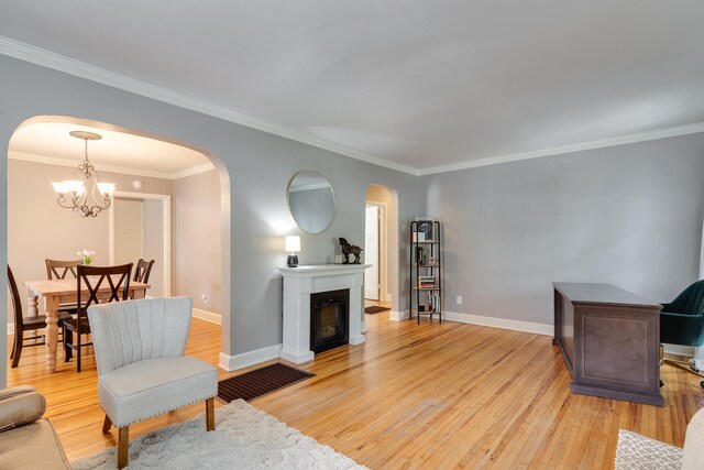 living area featuring crown molding, a notable chandelier, light wood-style floors, arched walkways, and baseboards