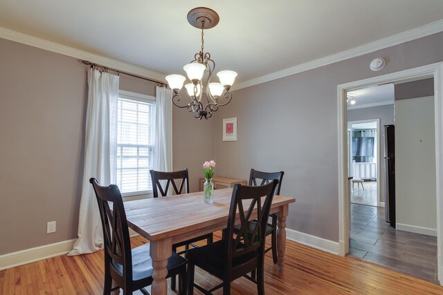 dining room featuring crown molding, baseboards, light wood-style flooring, and a notable chandelier