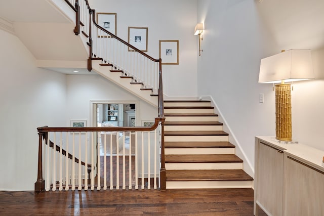 stairs featuring baseboards, wood finished floors, and a towering ceiling