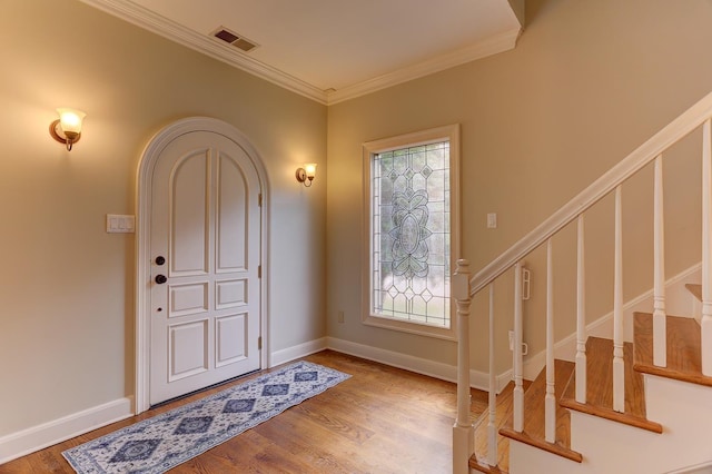 entryway with stairs, baseboards, wood finished floors, visible vents, and ornamental molding