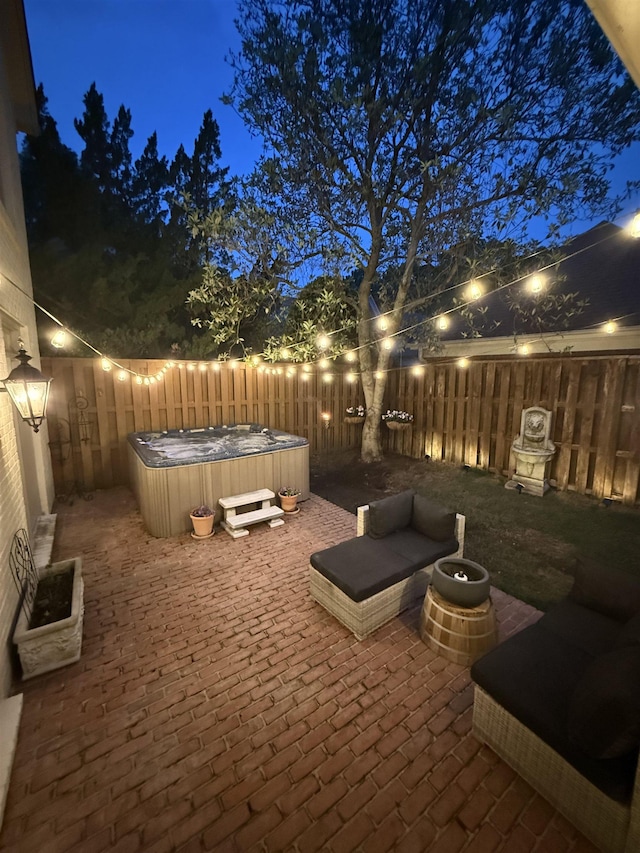patio at night featuring a fenced backyard and a hot tub