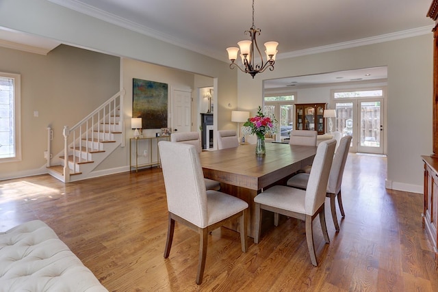 dining area featuring crown molding, an inviting chandelier, stairs, baseboards, and wood finished floors