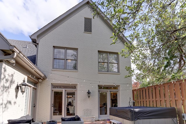 rear view of house featuring a hot tub, brick siding, and fence