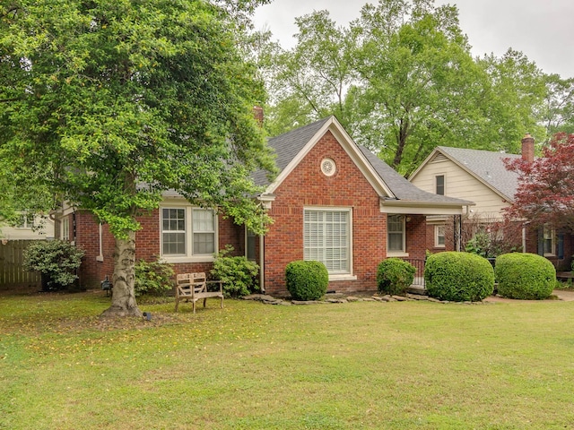 view of front of property featuring brick siding, a front lawn, roof with shingles, and fence
