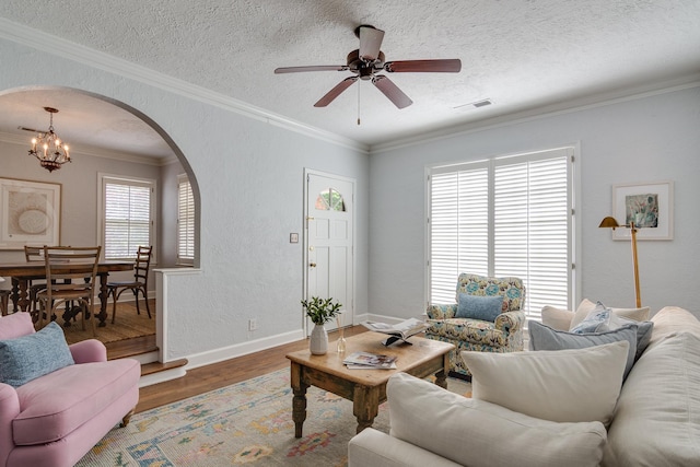 living room featuring arched walkways, ceiling fan with notable chandelier, baseboards, wood finished floors, and visible vents