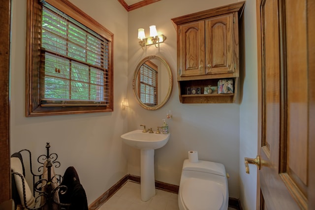 half bathroom featuring tile patterned flooring, crown molding, toilet, baseboards, and a sink
