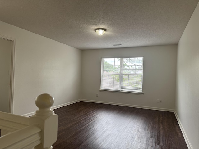 spare room with visible vents, a textured ceiling, dark wood finished floors, and baseboards