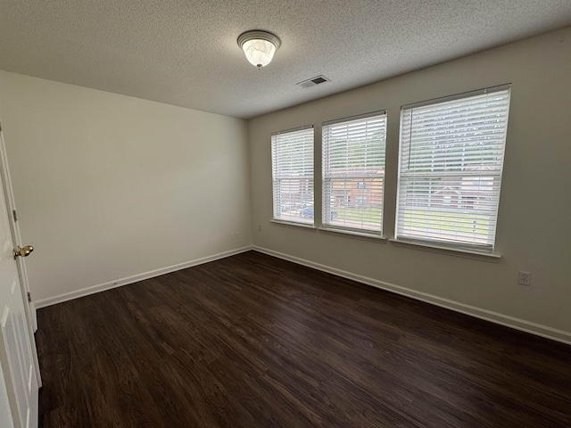 empty room with a textured ceiling, baseboards, visible vents, and dark wood-type flooring