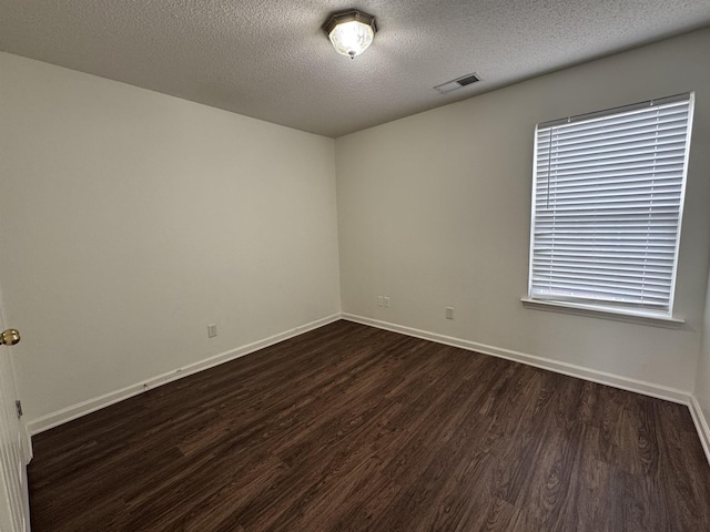 empty room featuring baseboards, dark wood-style flooring, a textured ceiling, and visible vents