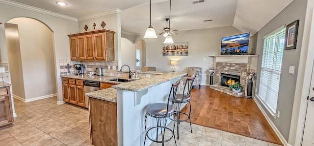 kitchen with brown cabinetry, a peninsula, plenty of natural light, arched walkways, and a sink