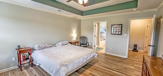 bedroom with crown molding, light wood-style floors, baseboards, a tray ceiling, and visible vents