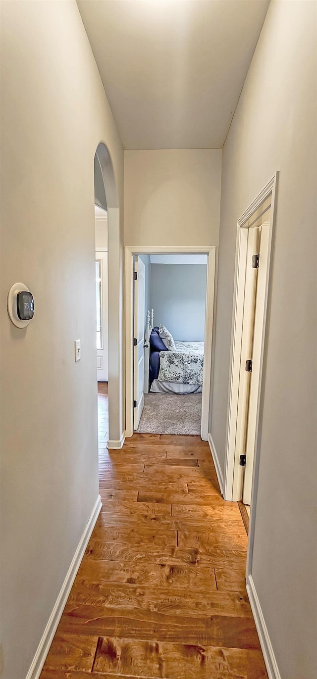 corridor featuring arched walkways, baseboards, and wood finished floors