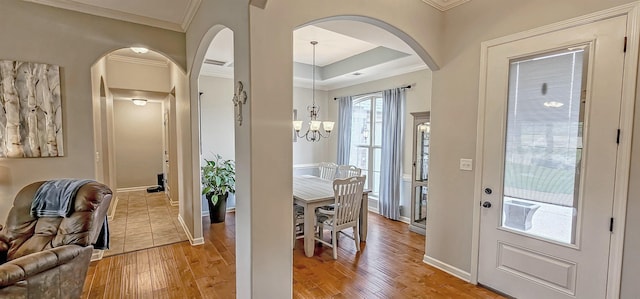 entryway with arched walkways, an inviting chandelier, ornamental molding, and light wood-style flooring