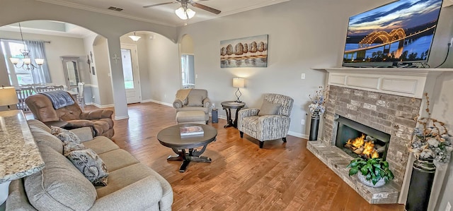 living area featuring visible vents, a brick fireplace, wood finished floors, arched walkways, and ceiling fan with notable chandelier