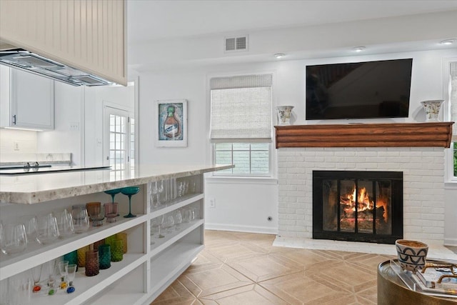 interior space featuring a brick fireplace, baseboards, visible vents, and plenty of natural light