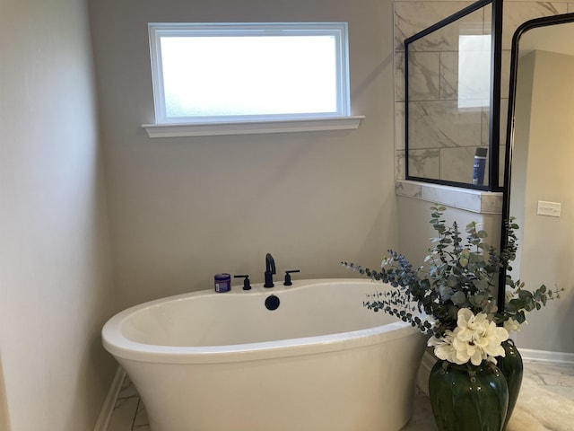 bathroom featuring baseboards, marble finish floor, a freestanding tub, and a healthy amount of sunlight