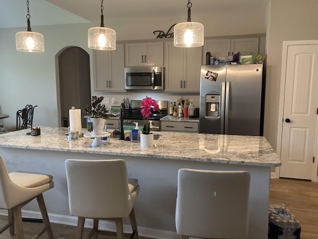 kitchen featuring a kitchen island with sink, arched walkways, hanging light fixtures, a breakfast bar, and stainless steel appliances