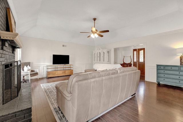 living room with dark wood finished floors, ceiling fan, wainscoting, and a fireplace