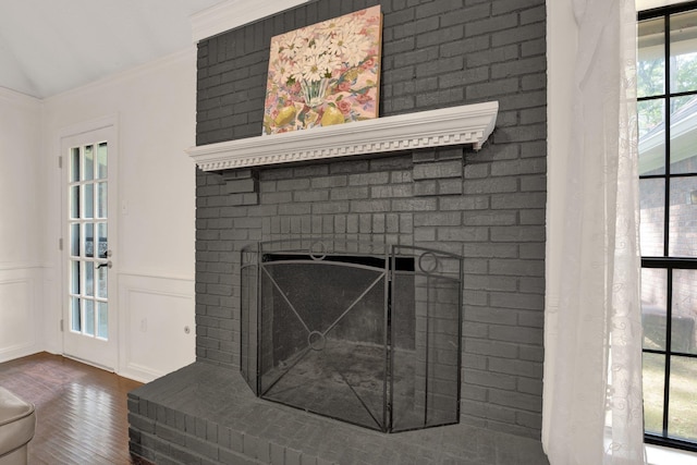 details featuring crown molding, wainscoting, a brick fireplace, wood finished floors, and a decorative wall