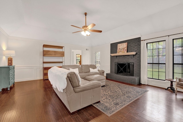 living room with ceiling fan, dark wood-style flooring, vaulted ceiling, a brick fireplace, and a wainscoted wall