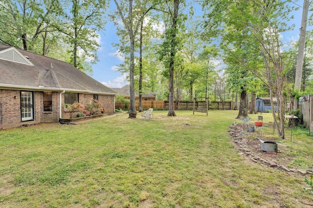 view of yard with an outbuilding, a fire pit, a fenced backyard, and a shed