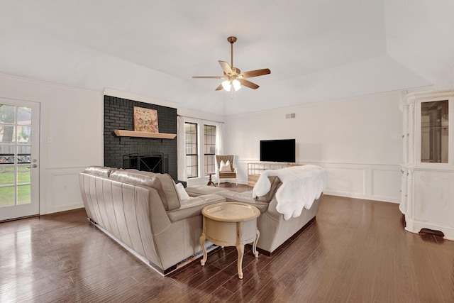living area with a brick fireplace, ceiling fan, wood finished floors, and a decorative wall